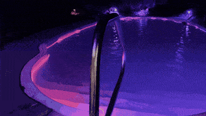 A swimming pool rimmed in glowing magenta and blue Trippy Wire at night.