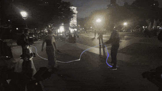 Two people turning a glowing jump rope of Trippy Wire in a city park at night.