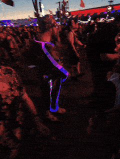 A festival-goer wearing glowing Trippy Wire, moving through a crowd at dusk.